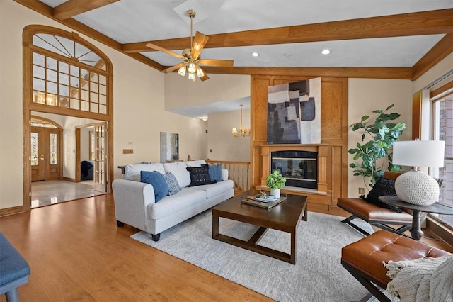 living area with vaulted ceiling with beams, light wood-style flooring, french doors, ceiling fan with notable chandelier, and a glass covered fireplace