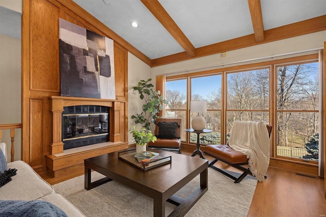 living room featuring beamed ceiling, light wood-style flooring, visible vents, and a glass covered fireplace