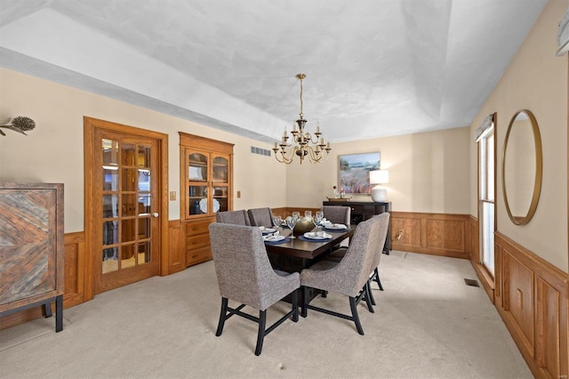 dining space with a notable chandelier, light colored carpet, visible vents, and wainscoting