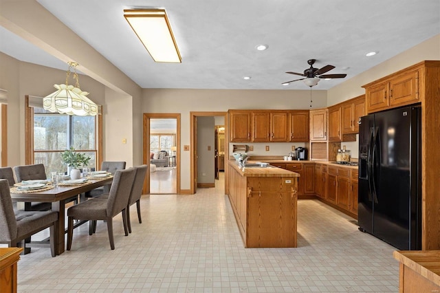 kitchen featuring brown cabinetry, recessed lighting, black fridge, and a sink