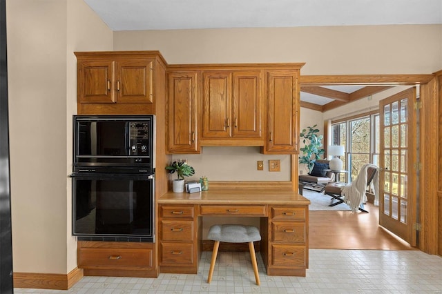 kitchen with baseboards, black microwave, light countertops, beam ceiling, and brown cabinetry