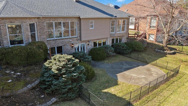 back of property with brick siding, roof with shingles, a yard, and fence