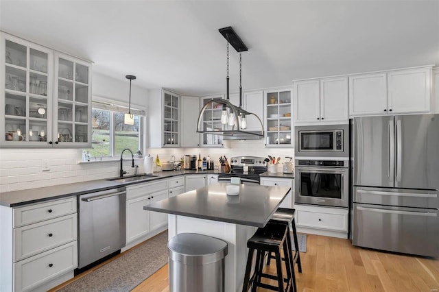 kitchen featuring a kitchen bar, a sink, tasteful backsplash, dark countertops, and stainless steel appliances