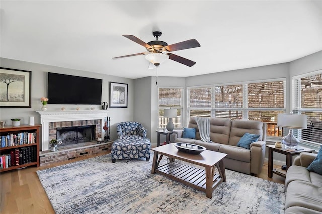 living area featuring a brick fireplace, baseboards, a ceiling fan, and wood finished floors