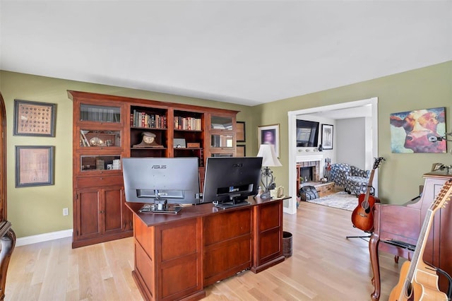 office with baseboards, a fireplace with raised hearth, and light wood finished floors