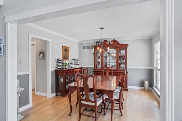 dining room featuring visible vents, baseboards, an inviting chandelier, light wood-style flooring, and crown molding