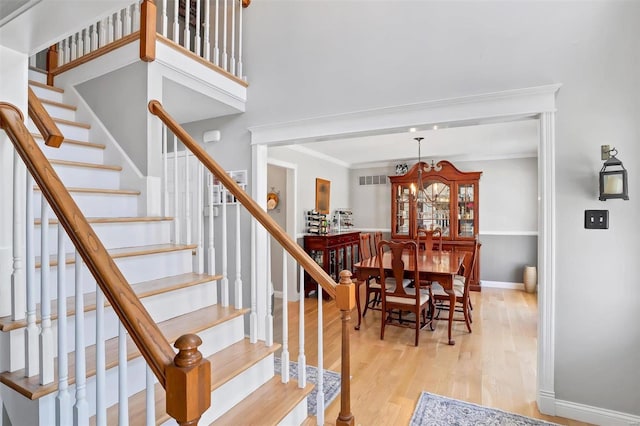 stairs featuring wood finished floors, visible vents, baseboards, ornamental molding, and a notable chandelier