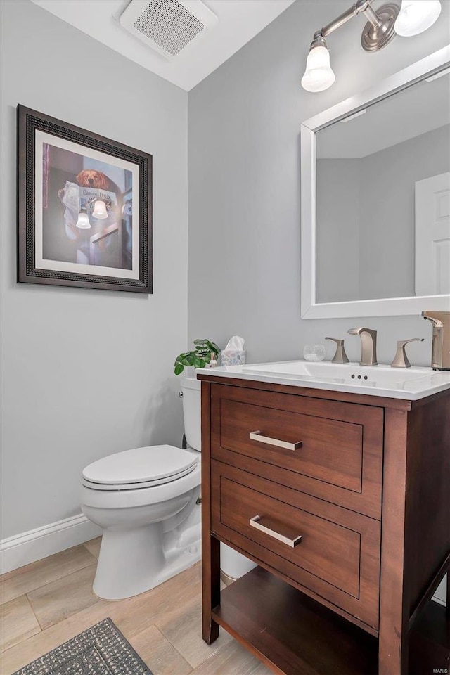 half bathroom featuring visible vents, baseboards, toilet, wood finished floors, and vanity