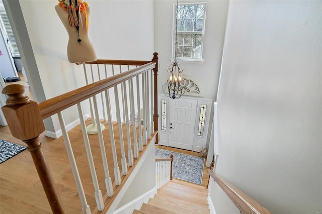 staircase with an inviting chandelier, wood finished floors, and baseboards