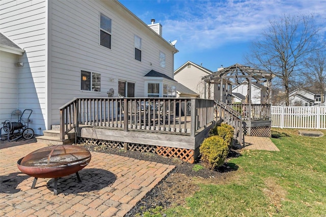 back of house with a deck, a patio, fence, a fire pit, and a chimney