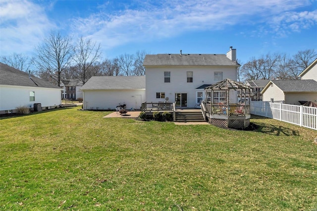 back of property featuring fence, a wooden deck, a yard, a chimney, and a fire pit