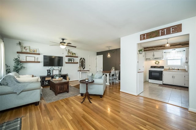 living area with baseboards, light wood-type flooring, and a ceiling fan