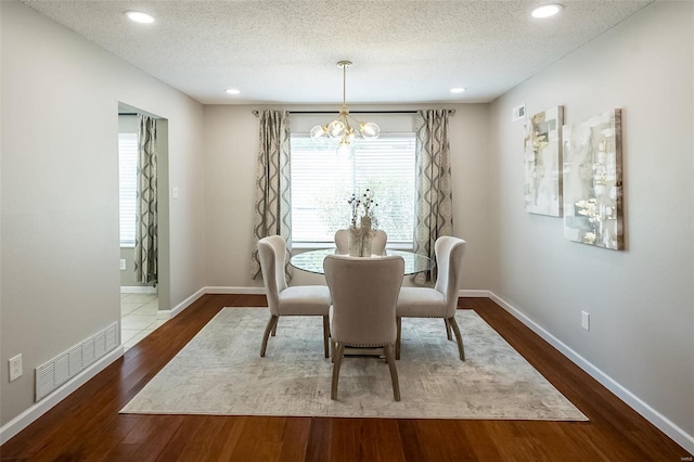 dining area featuring visible vents, a textured ceiling, an inviting chandelier, and wood finished floors