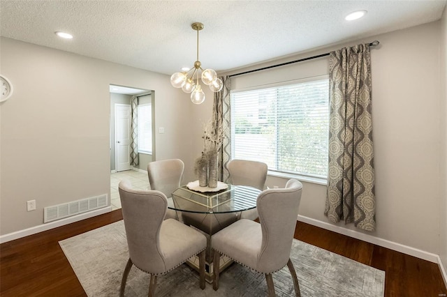 dining area featuring visible vents, baseboards, a chandelier, wood finished floors, and a textured ceiling