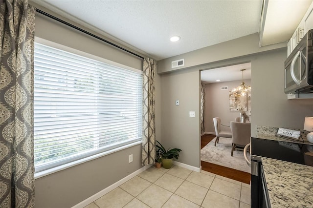 interior space with visible vents, baseboards, light tile patterned floors, a notable chandelier, and a textured ceiling