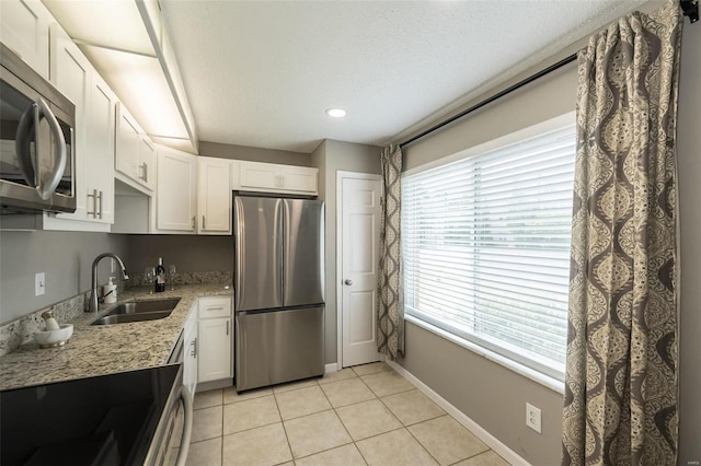 kitchen with a sink, stainless steel appliances, light tile patterned flooring, and white cabinets