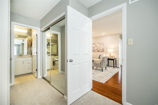 corridor with light wood finished floors, light carpet, a textured ceiling, and baseboards