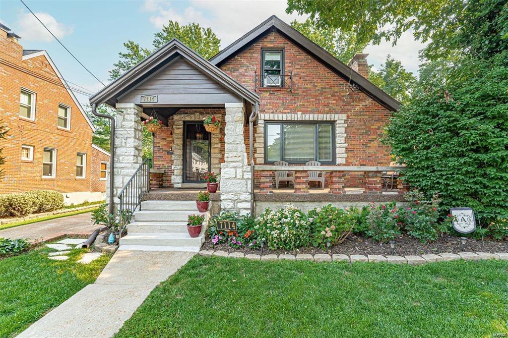 tudor house featuring covered porch, a chimney, a front lawn, stone siding, and brick siding