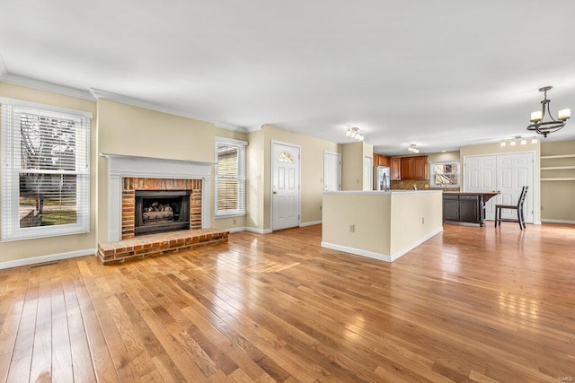 unfurnished living room with light wood-type flooring, ornamental molding, an inviting chandelier, a fireplace, and baseboards