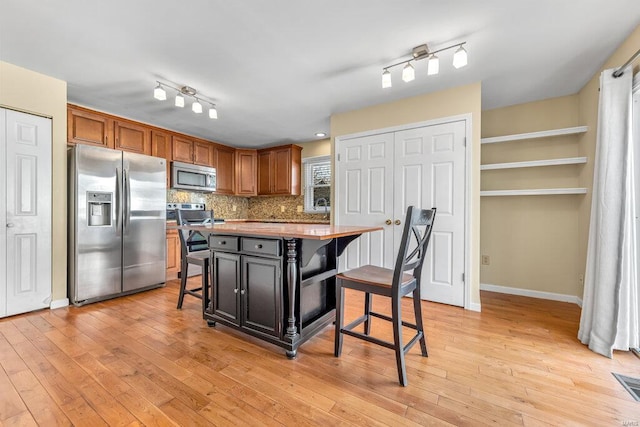 kitchen with a breakfast bar, tasteful backsplash, a center island, light wood-style floors, and appliances with stainless steel finishes