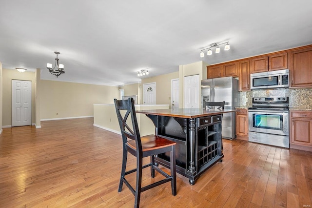 kitchen featuring baseboards, decorative backsplash, light wood-style flooring, brown cabinets, and stainless steel appliances