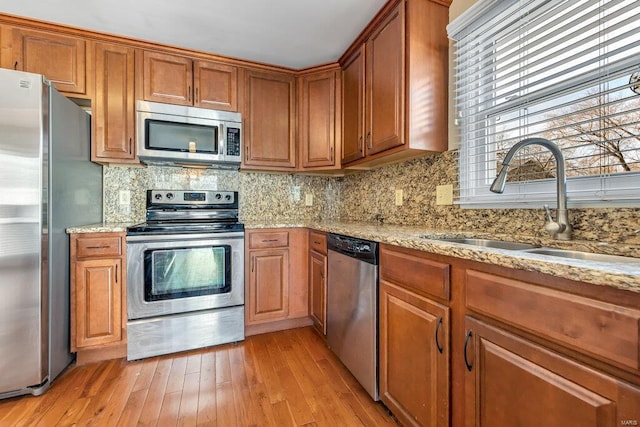 kitchen featuring light wood-type flooring, brown cabinets, a sink, backsplash, and stainless steel appliances