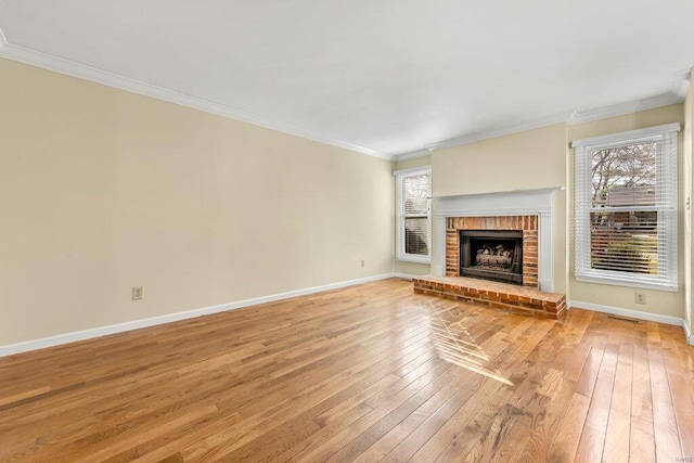 unfurnished living room with light wood-style flooring, a fireplace, crown molding, and baseboards