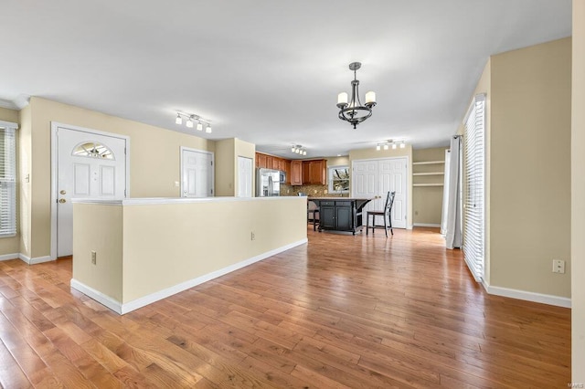 unfurnished living room with a notable chandelier, baseboards, light wood-style floors, and track lighting