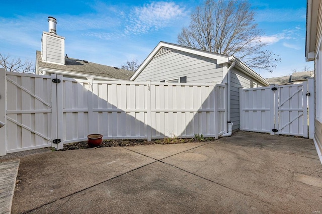 view of side of property with a patio, fence, a chimney, and a gate