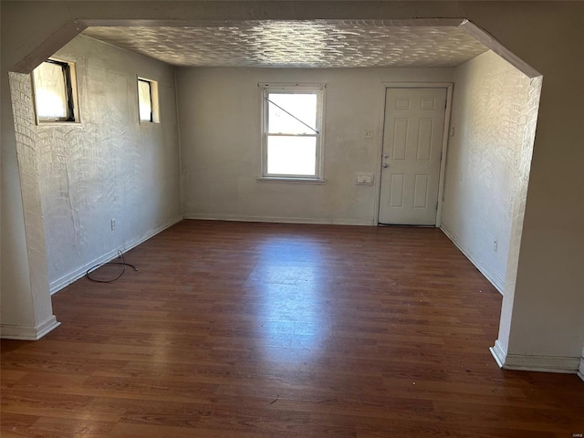 empty room featuring wood finished floors, baseboards, a textured wall, and arched walkways