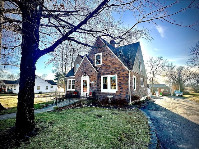 view of front of home with brick siding, driveway, a front yard, and a chimney