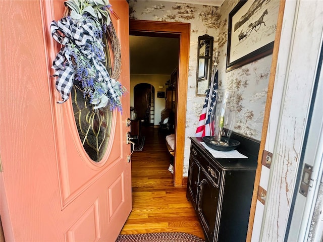 corridor featuring arched walkways, wallpapered walls, and light wood-style floors