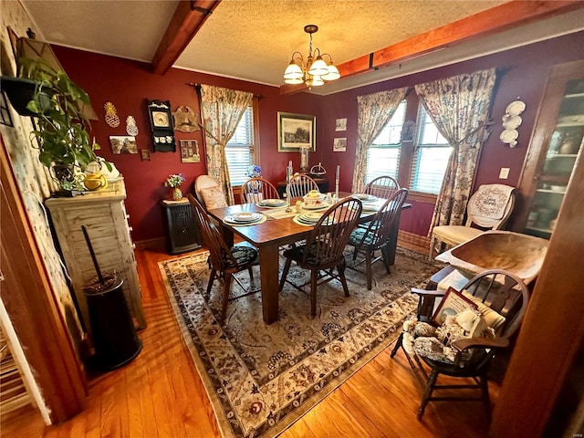 dining space featuring hardwood / wood-style floors, an inviting chandelier, a textured ceiling, beamed ceiling, and a wealth of natural light