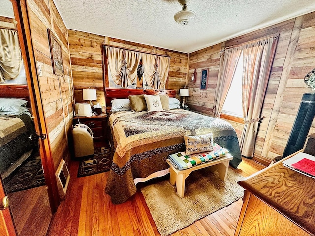 bedroom with wood-type flooring, visible vents, wood walls, and a textured ceiling