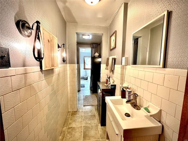 corridor with a sink, tile walls, light tile patterned flooring, and wainscoting