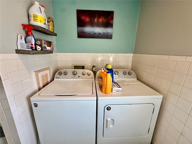 clothes washing area featuring separate washer and dryer, tile walls, wainscoting, and laundry area