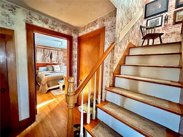 stairway featuring wallpapered walls and wood finished floors