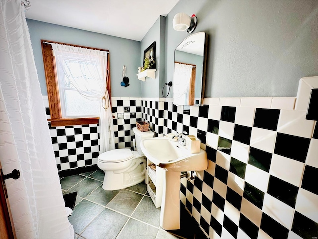 bathroom featuring tile patterned flooring, a wainscoted wall, toilet, and tile walls