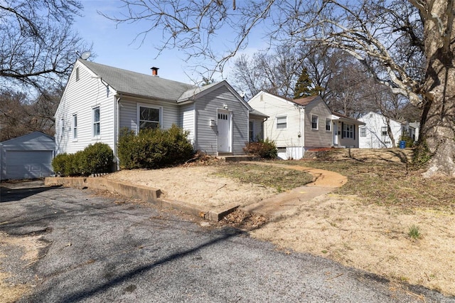 view of front of property featuring a garage, driveway, a chimney, and an outdoor structure