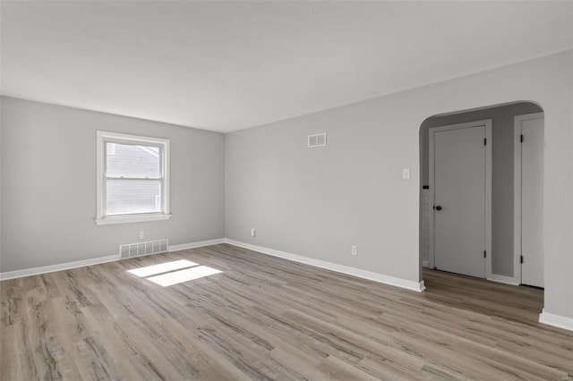 empty room featuring visible vents, arched walkways, baseboards, and wood finished floors