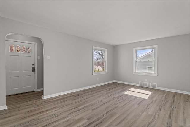 interior space with visible vents, arched walkways, baseboards, and wood finished floors