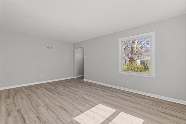 empty room with arched walkways, visible vents, baseboards, and wood finished floors