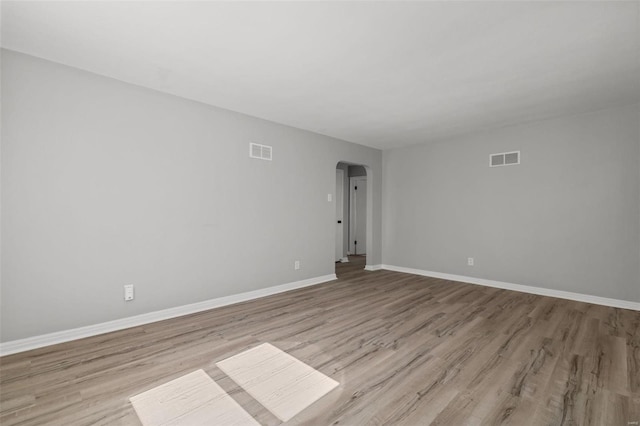 empty room featuring arched walkways, visible vents, baseboards, and wood finished floors