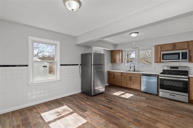 kitchen featuring dark wood-style floors, a sink, stainless steel appliances, light countertops, and tile walls