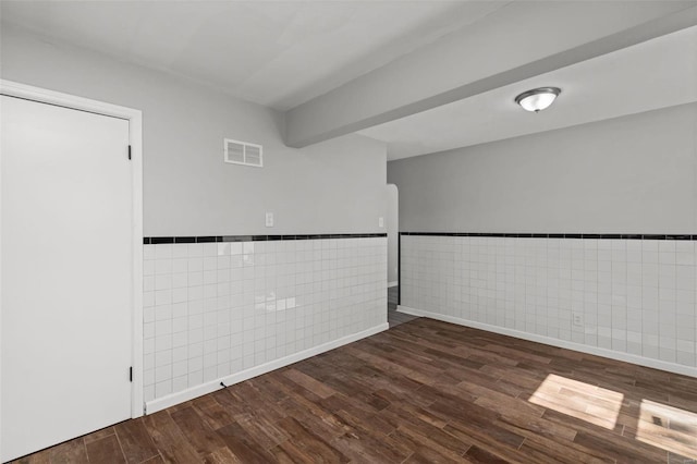 empty room with a wainscoted wall, tile walls, wood finished floors, and visible vents