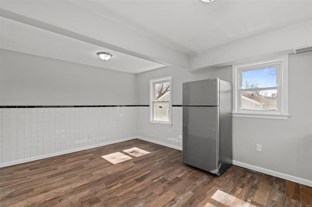 unfurnished room featuring visible vents, dark wood finished floors, tile walls, wainscoting, and baseboards