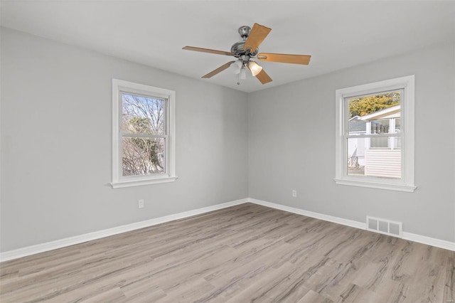 unfurnished room featuring a wealth of natural light, visible vents, light wood-type flooring, and baseboards