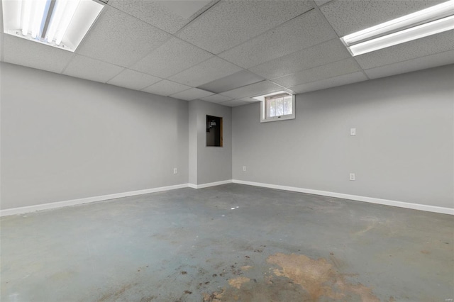 basement with a paneled ceiling and baseboards