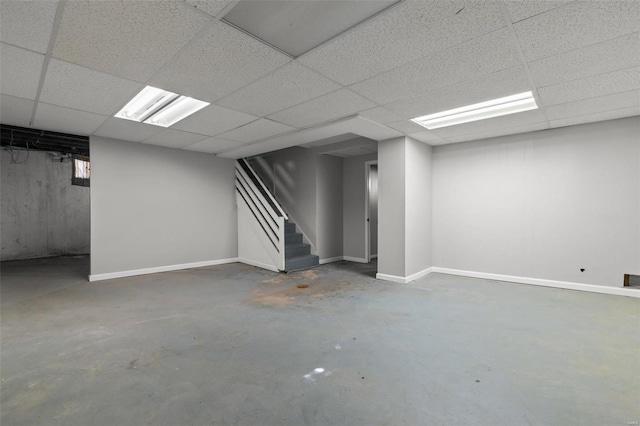 finished below grade area featuring a paneled ceiling, stairway, and baseboards