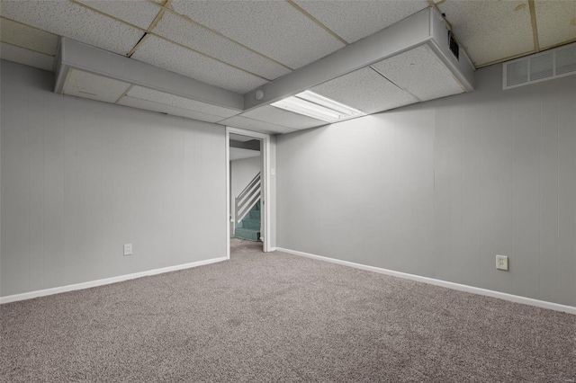 finished basement with visible vents, a drop ceiling, stairway, carpet, and baseboards